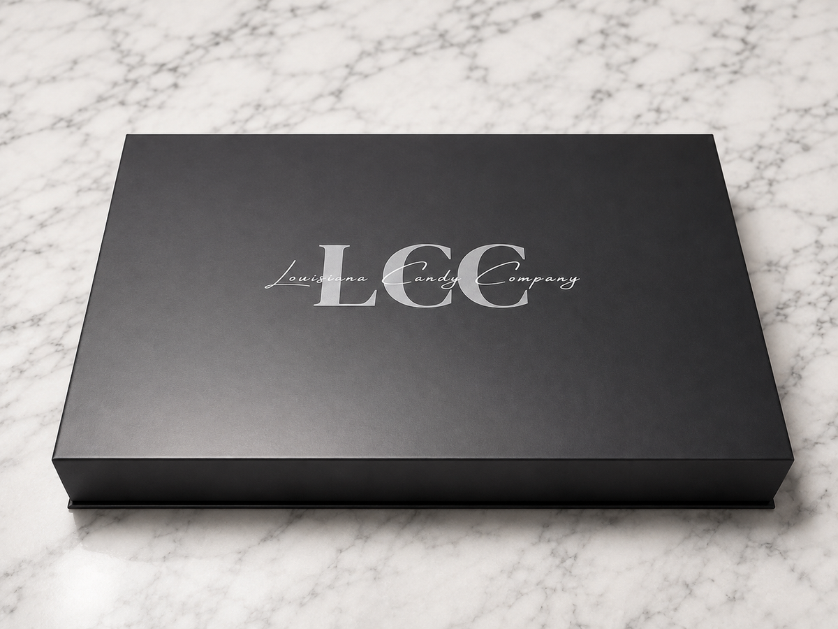 A black rectangular presentation box with the silver logo 'LCC Louisiana Candy Company' on the lid, photographed on a white marble surface.